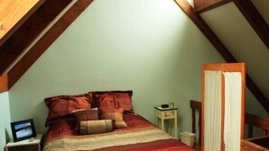 A bedroom with a sloped ceiling, a bed with a striped blanket, a bedside table with a lamp, and a window with curtains. - Pendletonheim 23 (Davis)