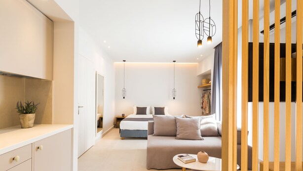 A modern hotel room with a minimalist design, featuring a bed, a sofa, a small table, and a kitchen area. - Calmare (Rethymno)
