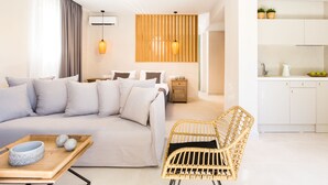 A modern hotel room with a large bed, a wicker chair, a wooden side table, and a kitchenette. - Calmare (Rethymno)
