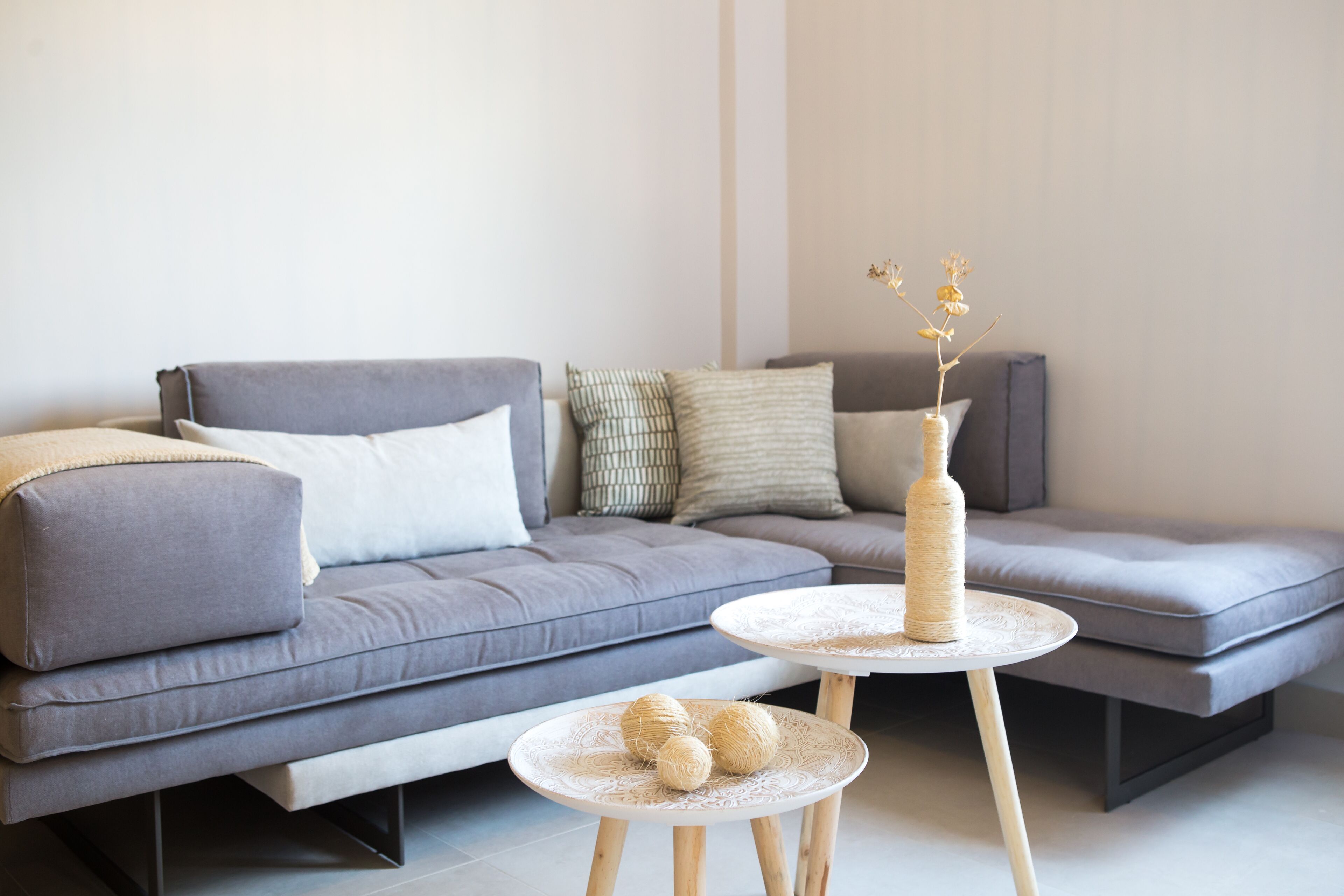 Una sala de estar moderna con un sofá seccional gris, una mesa de centro redonda con un adorno tejido y una mesita auxiliar pequeña.