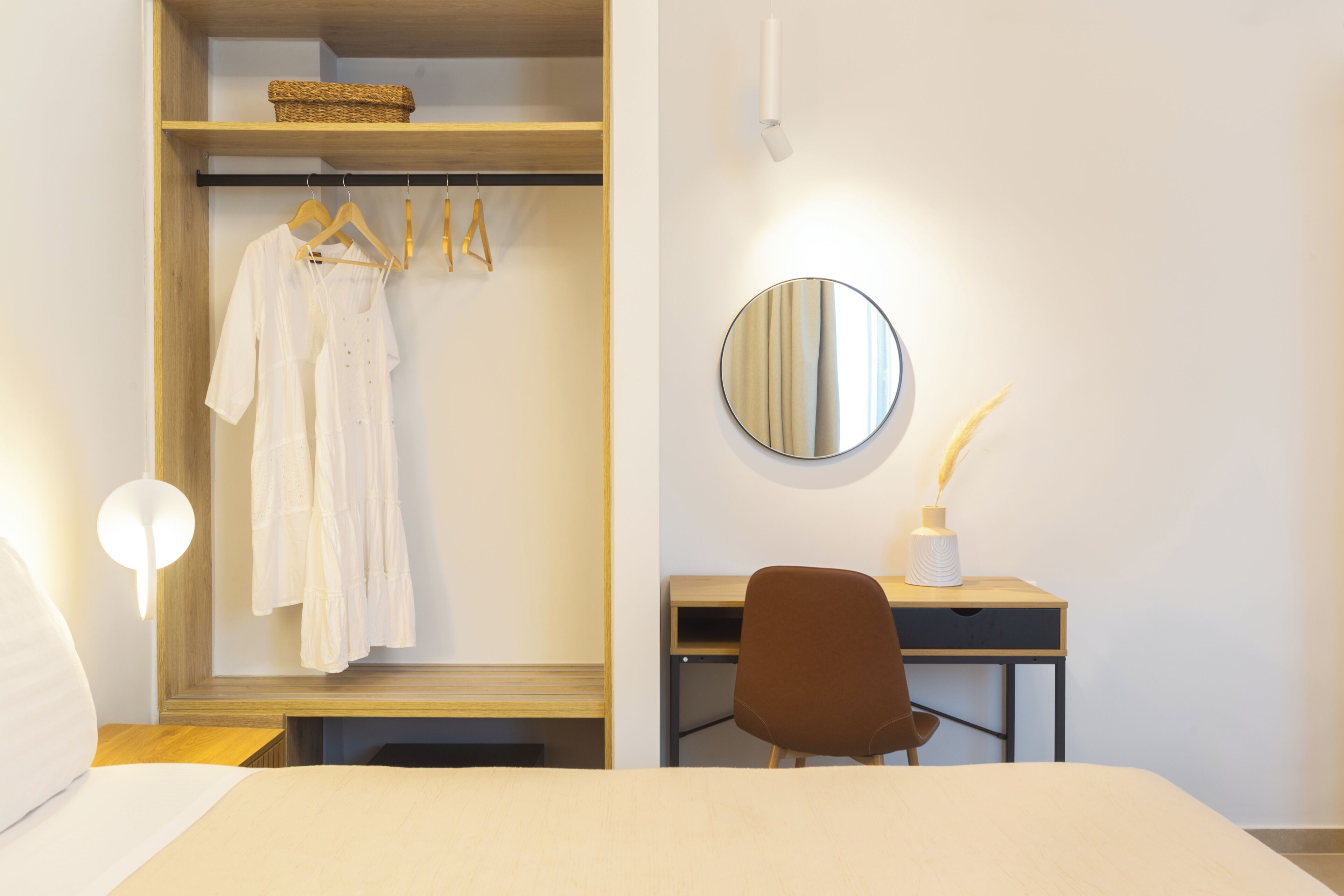Una habitación de hotel con cama, escritorio con silla, armario, espejo y lámpara de noche.