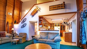 A cozy living room with a blue sofa, wooden coffee table, and a staircase leading to a kitchen area. - Paradise Found (Davis)