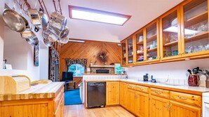 A kitchen with wooden cabinets, a dishwasher, and a dining area with a wooden table and chairs. - Paradise Found (Davis)