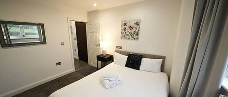 Habitación de hotel con una cama grande, una mesita de noche con lámpara, una ventana con vistas y una puerta que da a otra habitación.