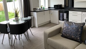 A modern kitchen with a dining area, a sofa, and a view of the garden. - The Hatton Apartments (Feltham)