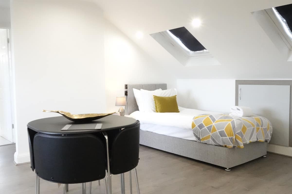 A modern bedroom with a bed, a small round table, and a skylight.