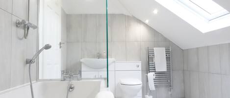 Un baño moderno con tragaluz, una bañera, un inodoro y un lavamanos.