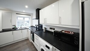 A modern kitchen with white cabinets, a black countertop, a washing machine, and a microwave. - The Hatton Apartments (Feltham)
