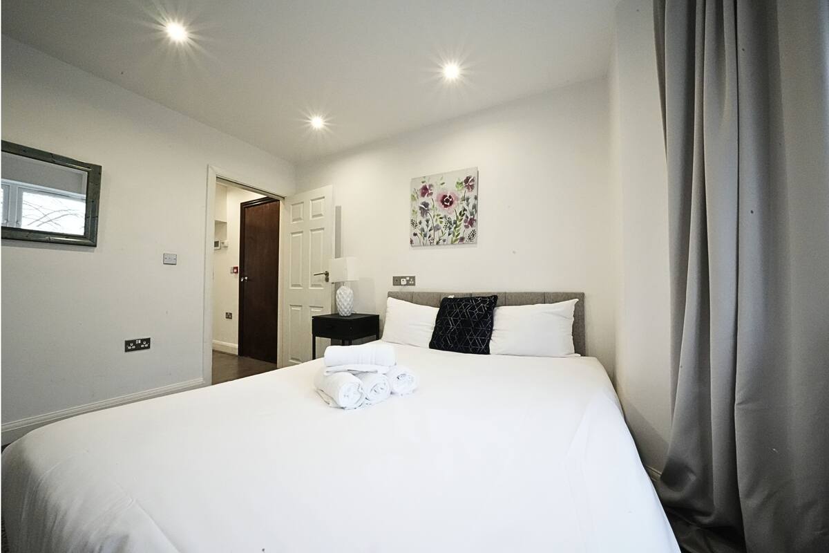 A hotel room with a large bed, a nightstand, a painting, and a window with a view.