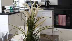 A modern kitchen with white cabinets, a black stove, and a dining area with a table set for two. - The Hatton Rooms (Feltham)