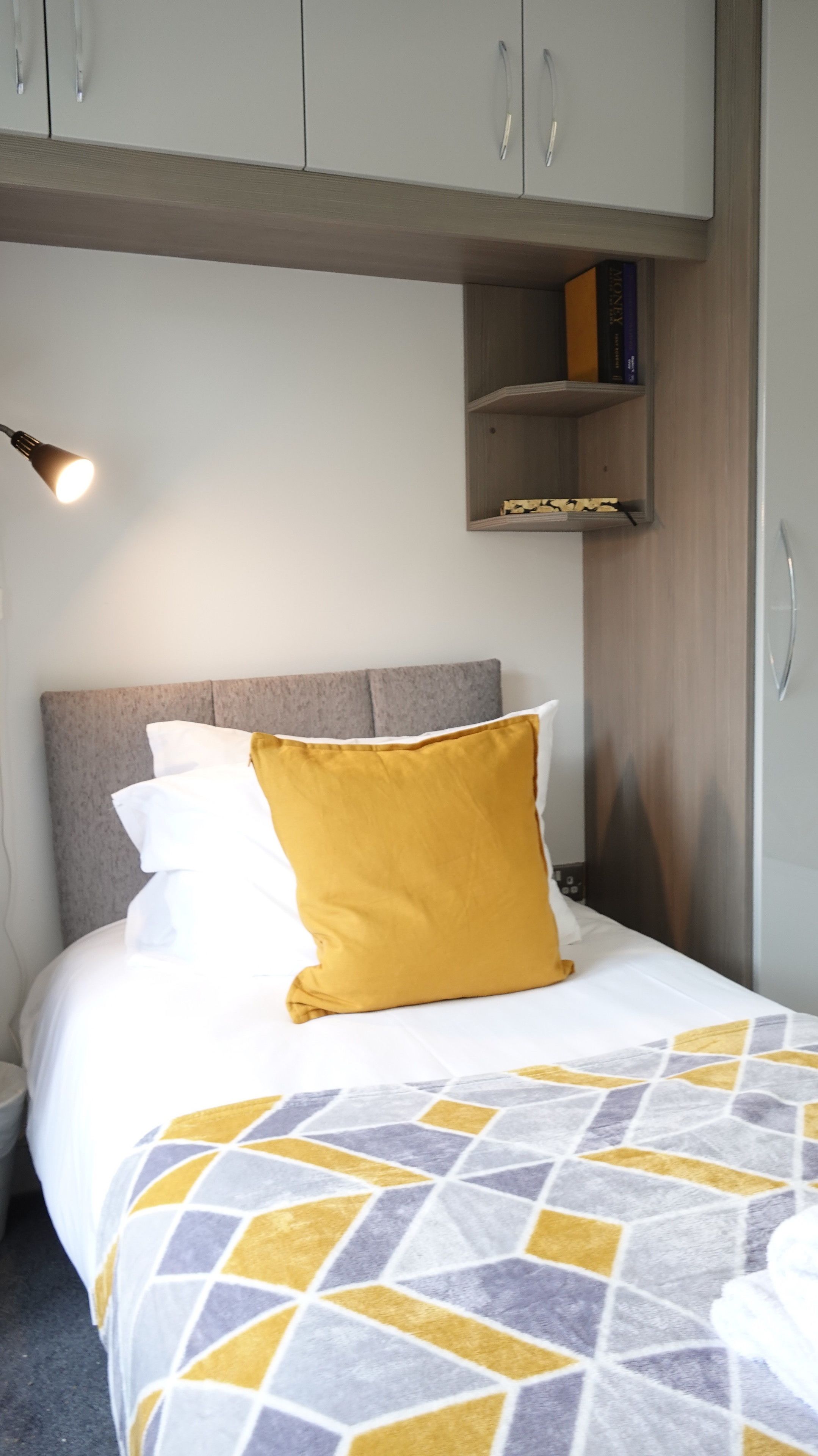 Un dormitorio con cama, mesita de noche, lámpara, armario y estante con libros.