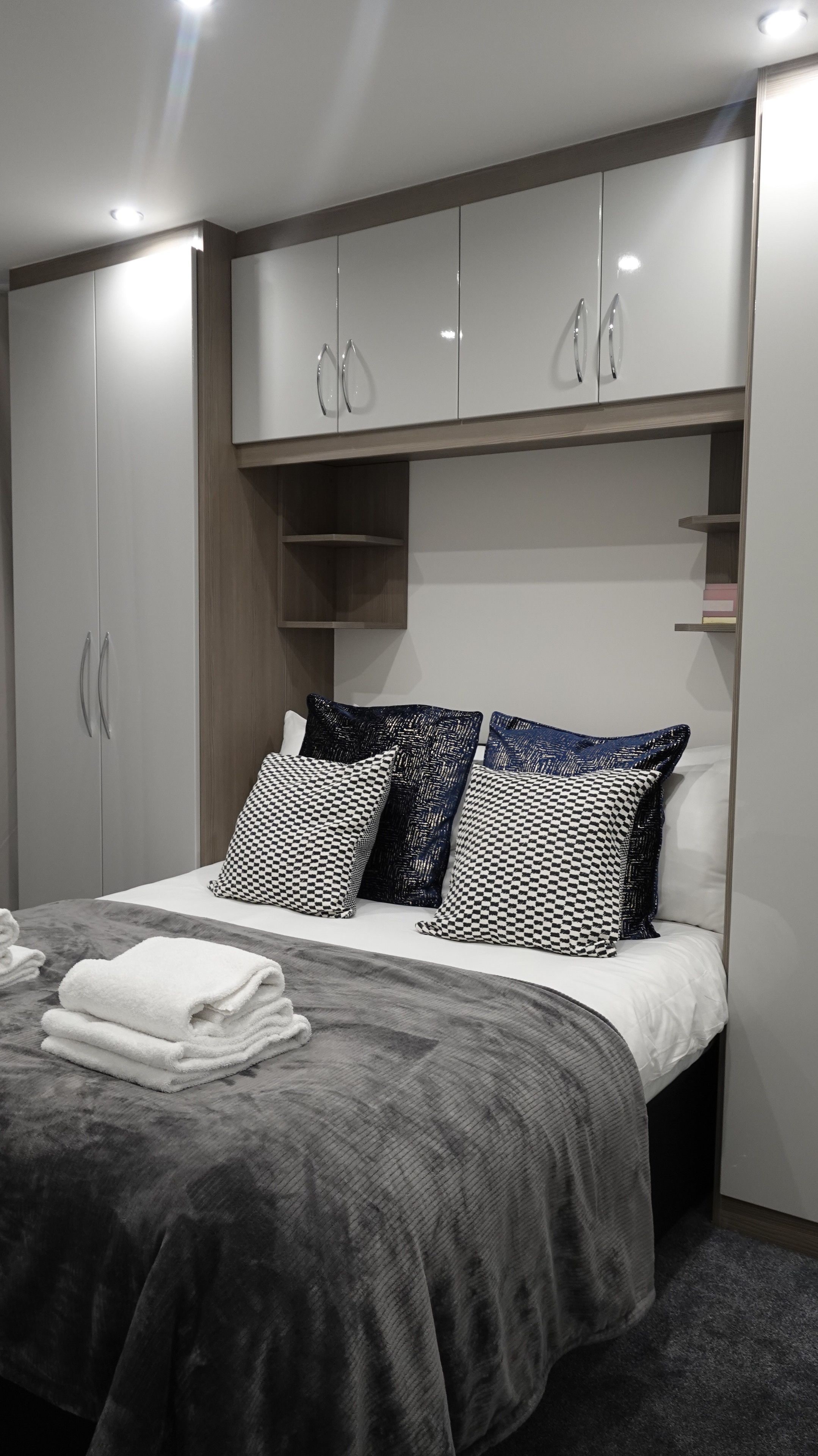 A modern bedroom with a bed, grey bedding, checkered pillows, and a wardrobe with mirrored doors.