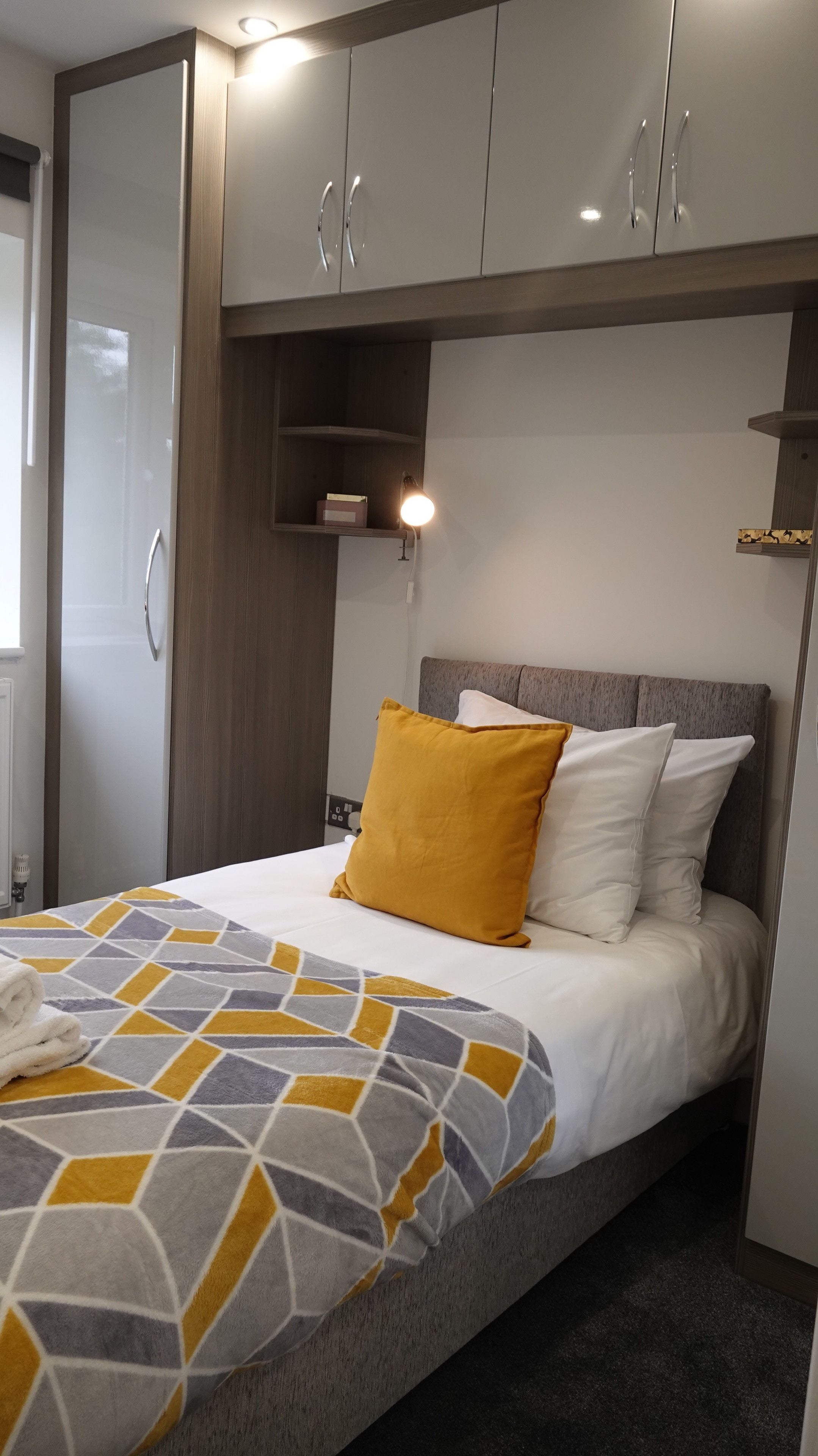 A bedroom with a bed, a nightstand, a wardrobe, and a shelf with a lamp.