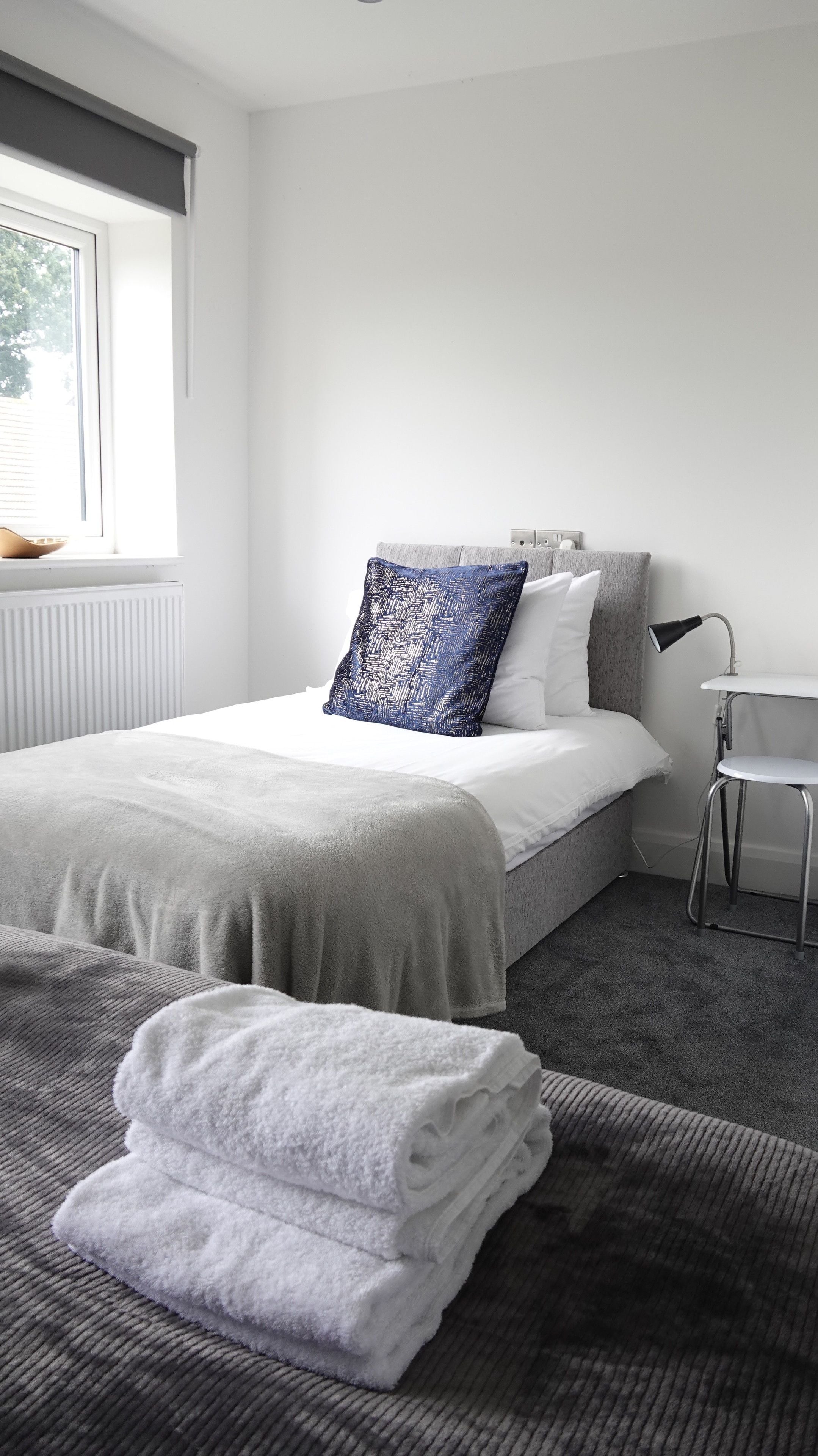 Quarto moderno com cama, mesa de cabeceira, luminária e vista para o exterior.