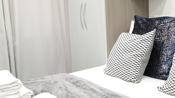 A modern hotel room with a neatly made bed, a wooden headboard, and a built-in wardrobe with a mirror. - The Hatton Rooms (Feltham)