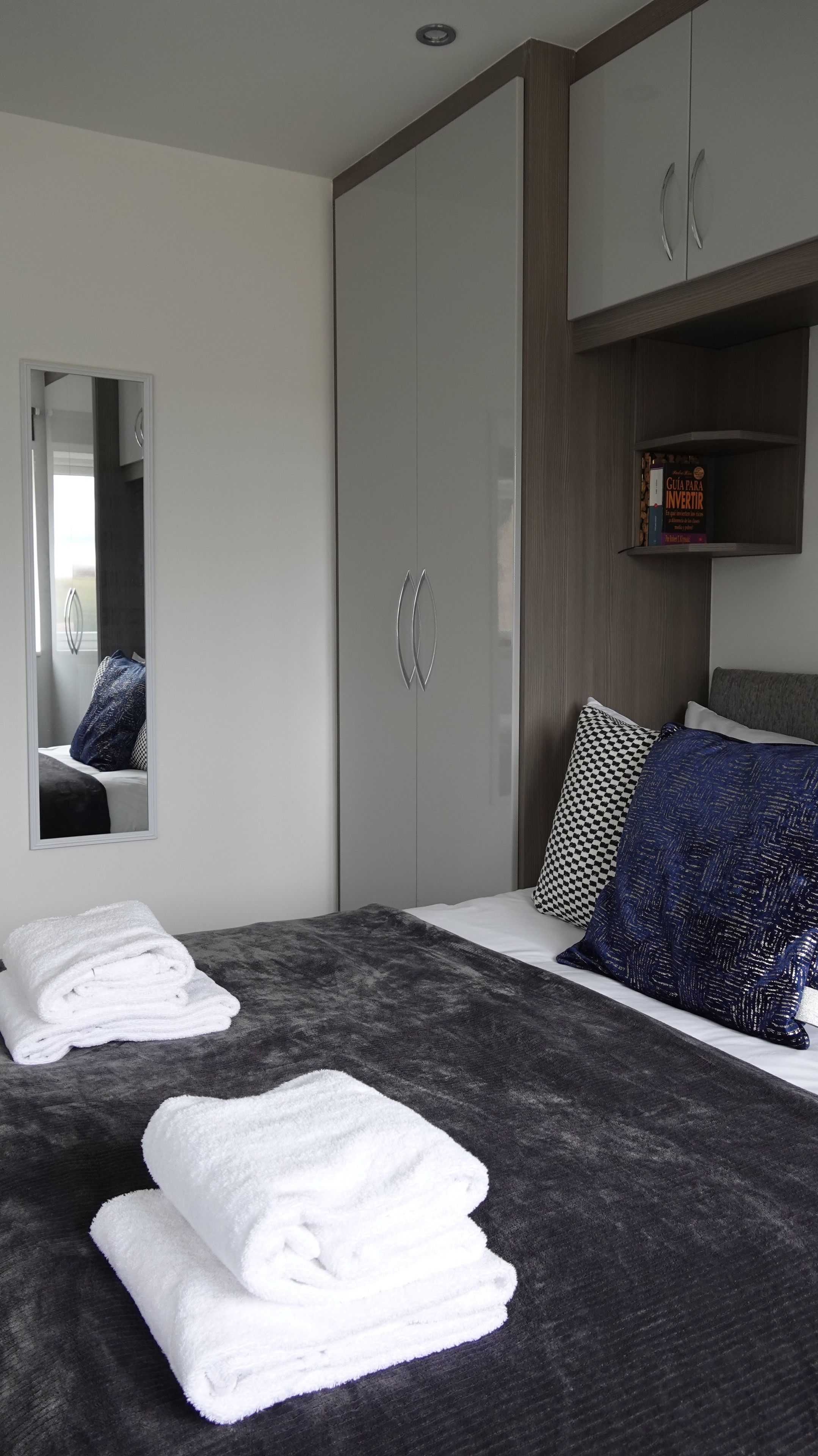 Quarto com uma cama, guarda-roupa, espelho e uma estante com livros.