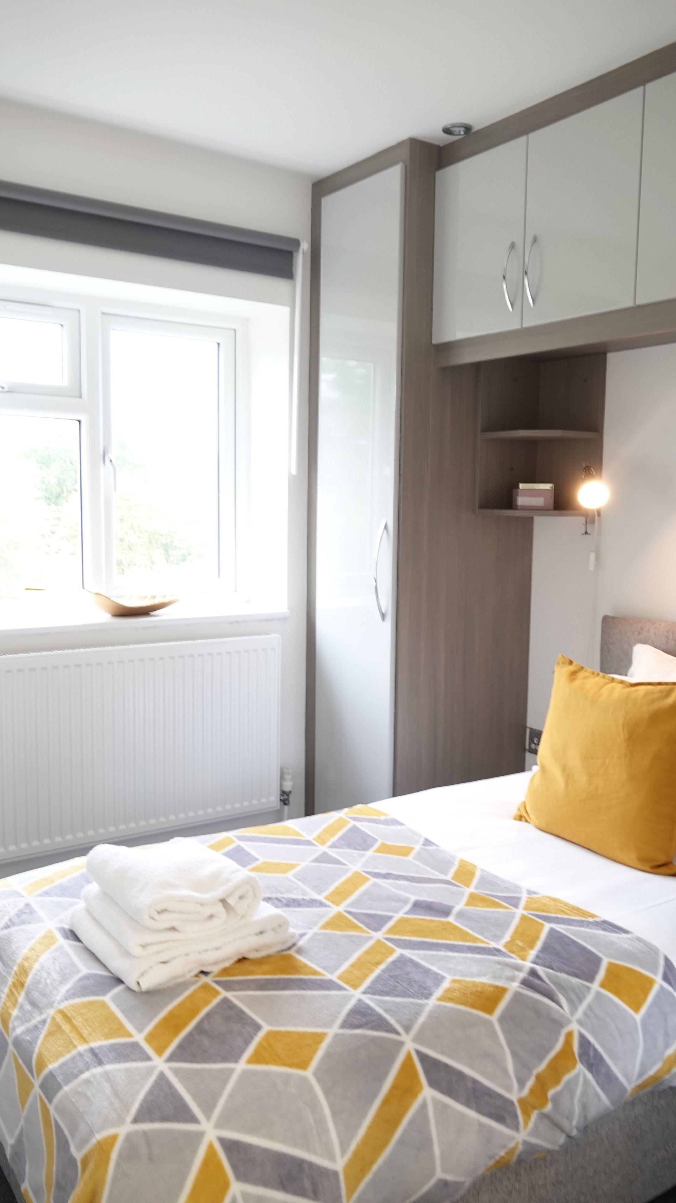 Une chambre à coucher avec un lit, une fenêtre, une armoire et une table de chevet avec une lampe.