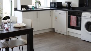 A modern kitchen with white cabinets, a black countertop, and a dining area with a table and chairs. - The Hatton Rooms (Feltham)