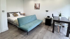 A modern, well-lit room with a bed, a blue sofa, a dining table, and a small side table. - The Hatton Rooms (Feltham)