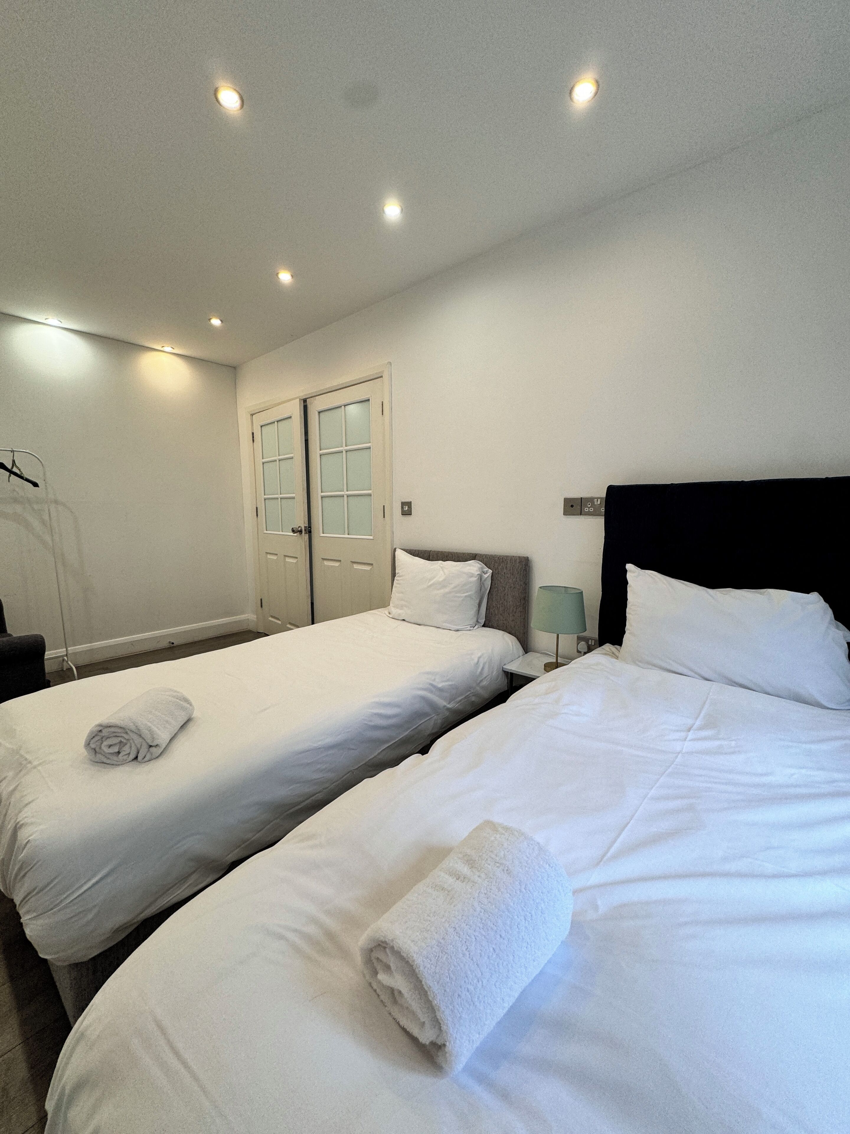 A hotel room with two single beds, a wardrobe, a mirror, and a hanging coat rack.