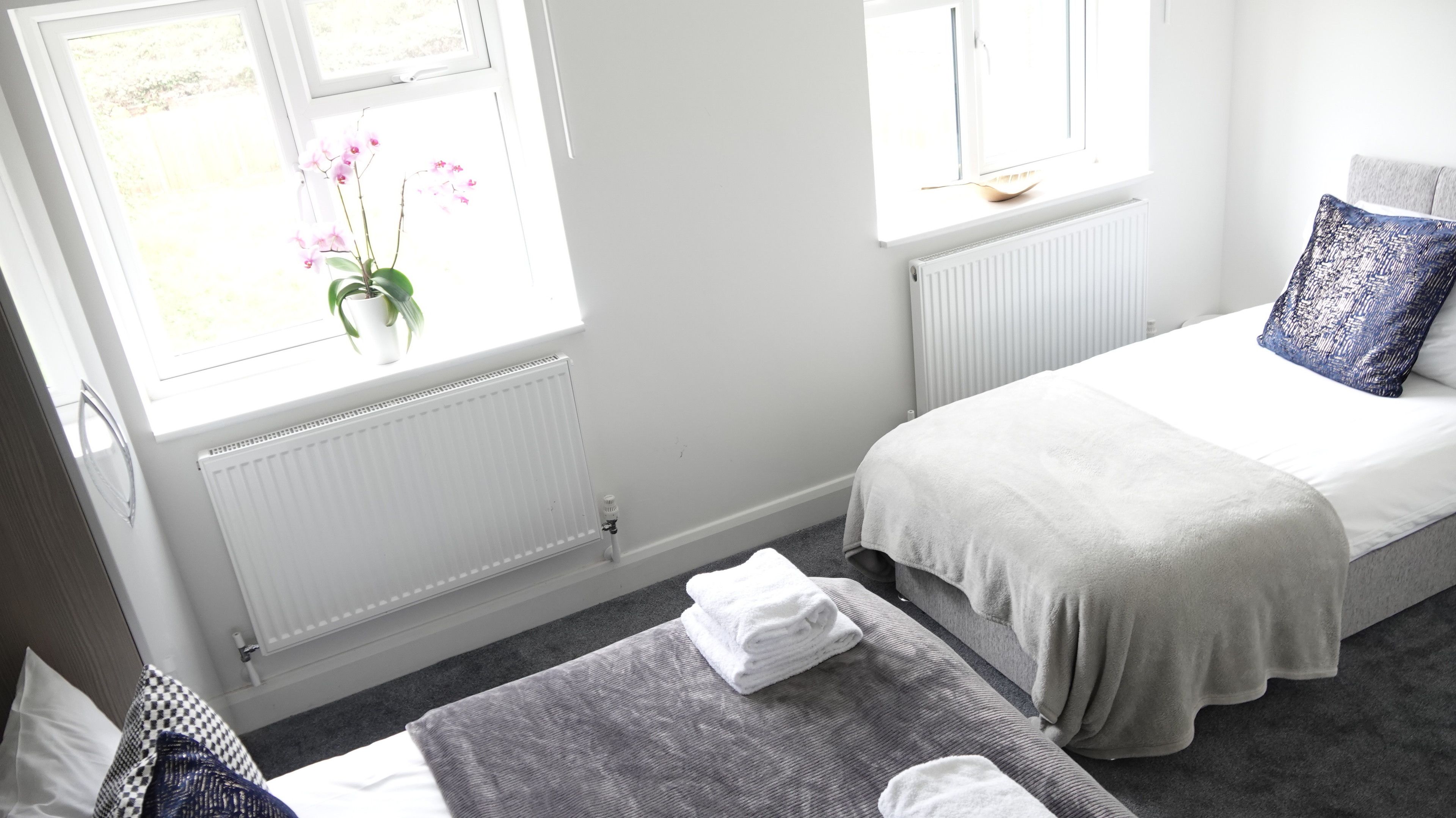 A hotel room with a bed, a bedside table, a window with a view of the outdoors, and a radiator.