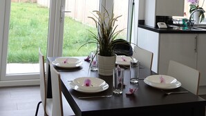 A dining area with a table set for four, a potted plant, and a view of a backyard through large sliding glass doors. - The Hatton Rooms (Feltham)