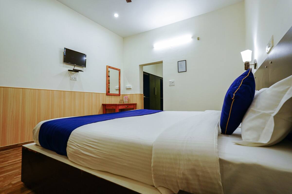 Een hotelkamer met een bed, een aan de muur bevestigde televisie, een spiegel en een deur naar een andere kamer.