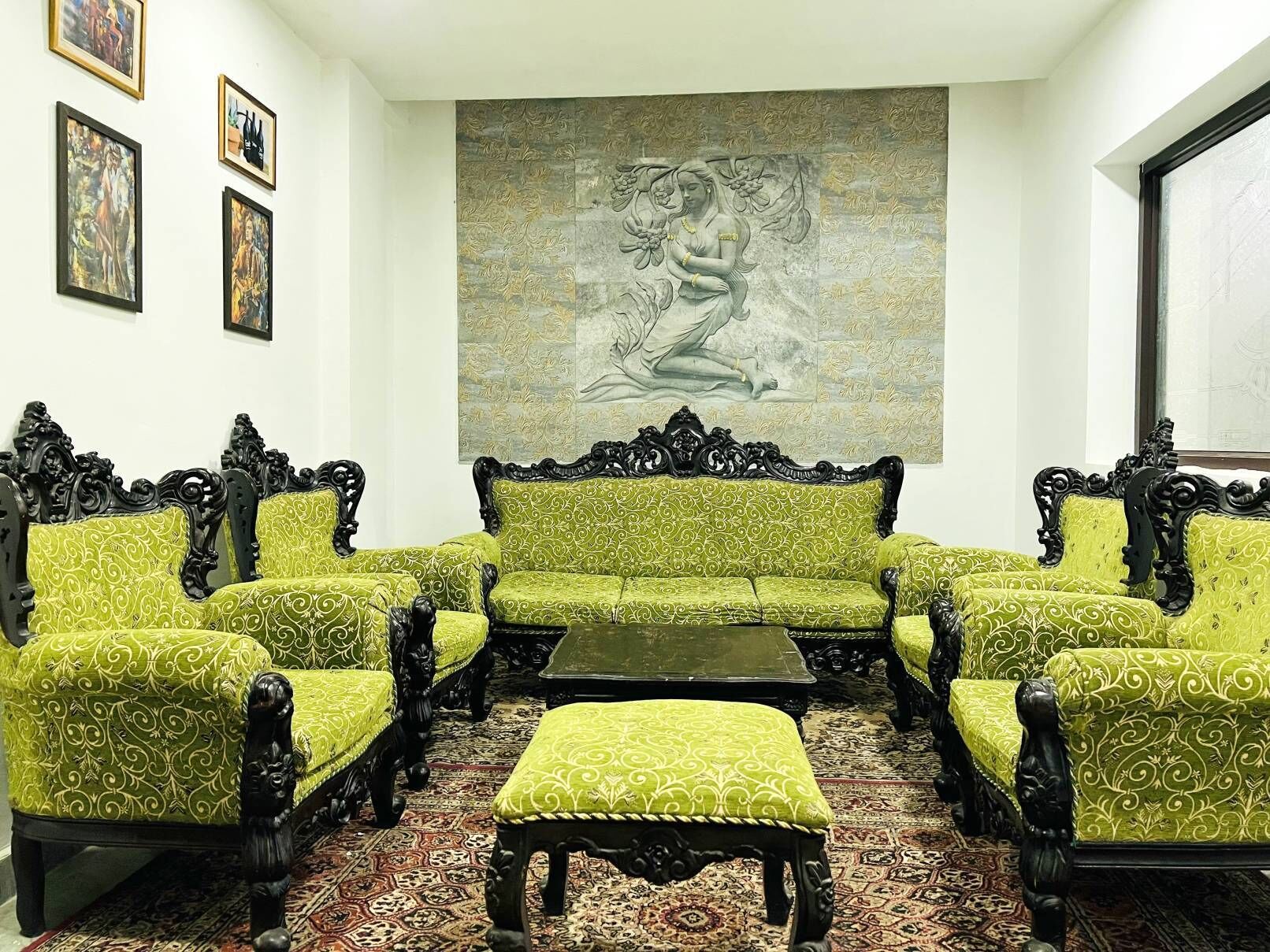 A room with a green patterned sofa set, a matching ottoman, and a large wall mural.