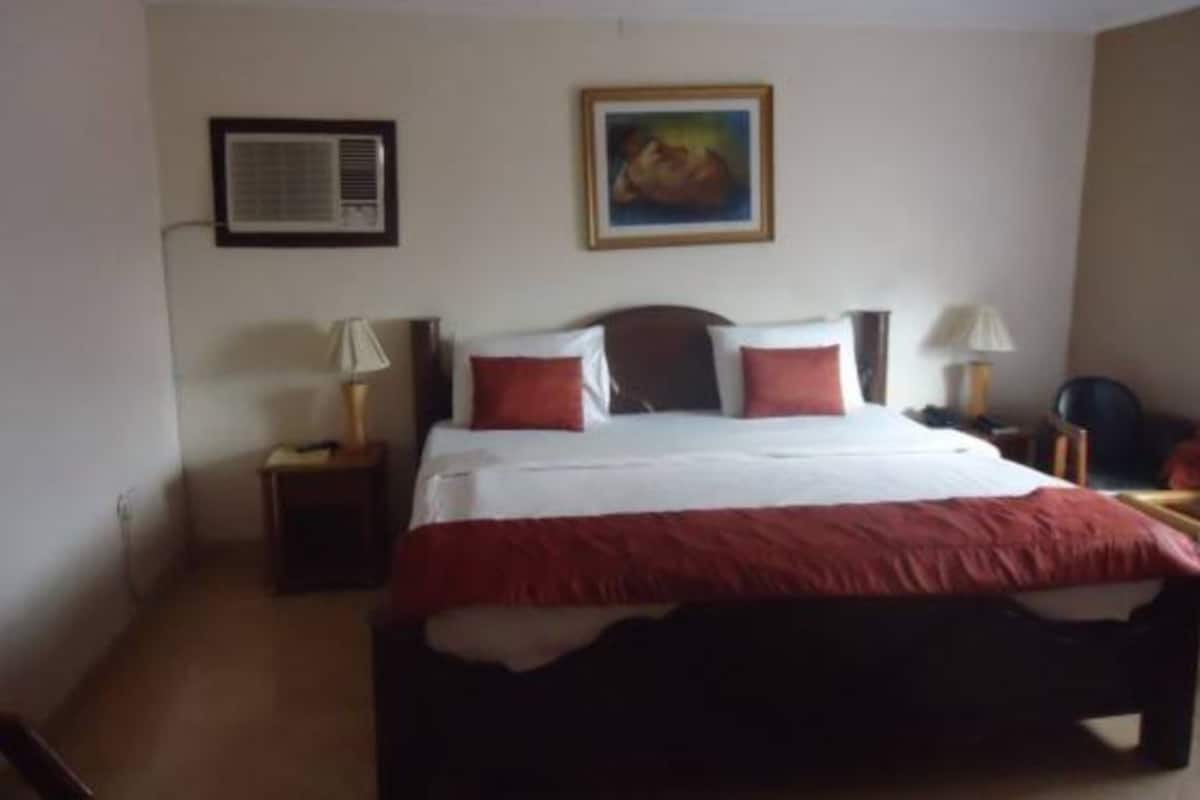 Habitación de hotel con cama, dos mesitas de noche, aire acondicionado de pared y un cuadro enmarco.