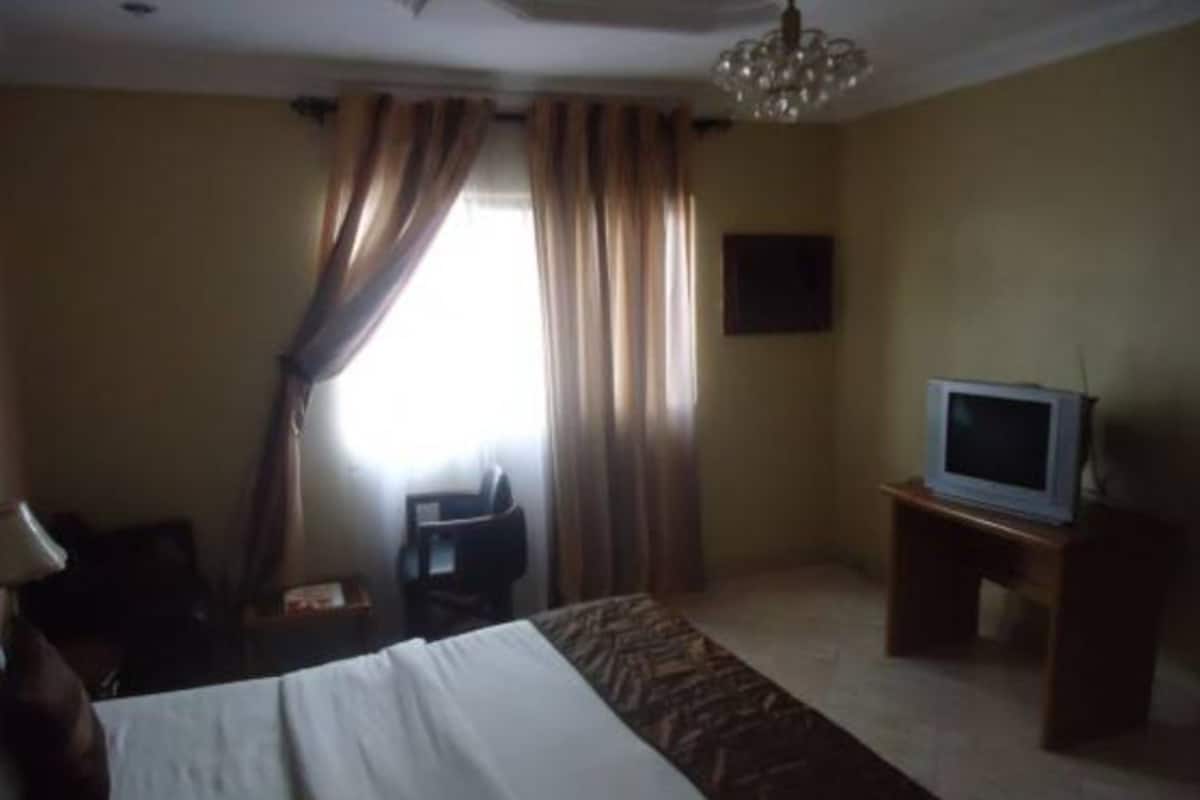 Una habitación de hotel con cama, televisor en un mueble, escritorio y una silla.