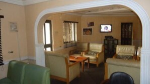 A living room with a green sofa, two armchairs, a coffee table, and a television. - Meridian Lodge hotels & resorts (Benin City)