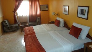 A hotel room with a large bed, two chairs, a small table, and a TV on the wall. - Meridian Lodge hotels & resorts (Benin City)