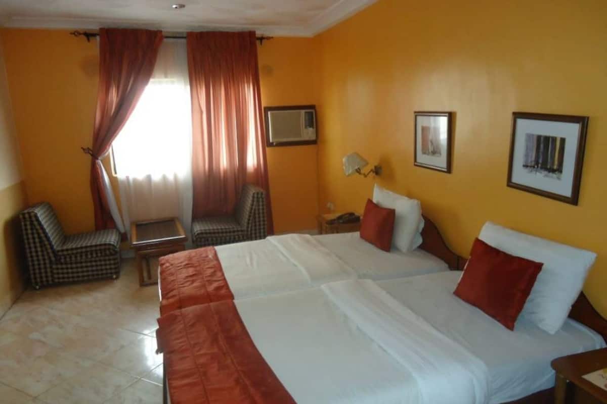 Una habitación de hotel con una cama grande, dos sillas, una mesita y un televisor en la pared.