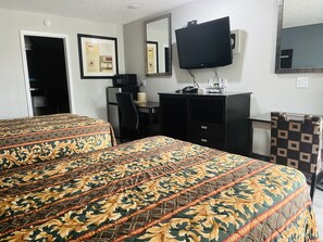 Una habitación de hotel con dos camas, un escritorio, una silla, un televisor y un espejo.