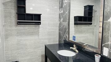 A bathroom with a black countertop, a white sink, a mirror, and a trash bin.