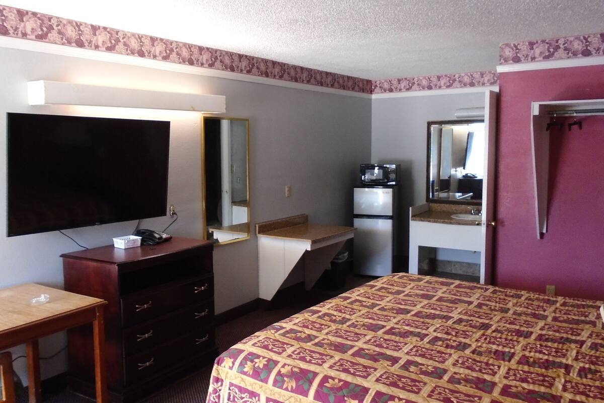 Een hotelkamer met een bed, een bureau, een dressoir, een televisietoestel, een koelkast, een magnetron en een badkamer met een wastafel en spiegel.