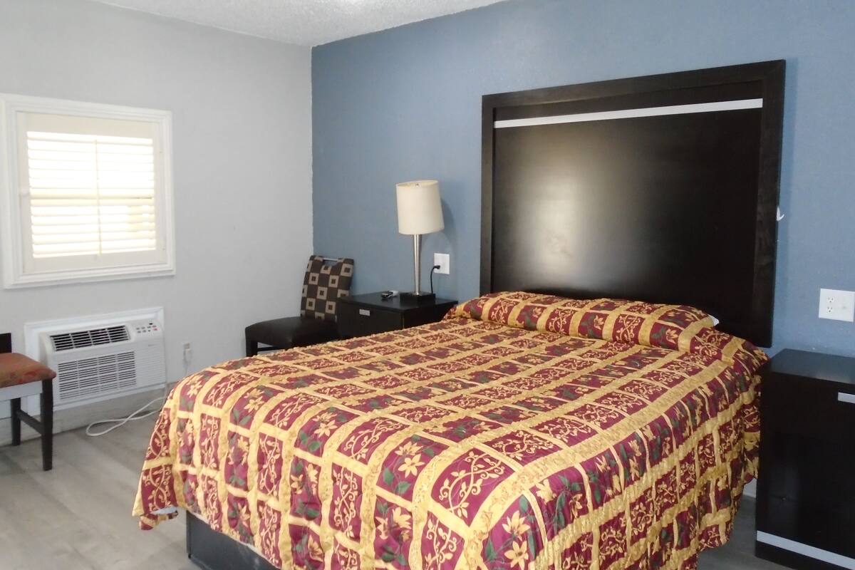 Een slaapkamer met een groot bed, een nachtkastje, een lamp, een raam met zonwering en een airconditioning.