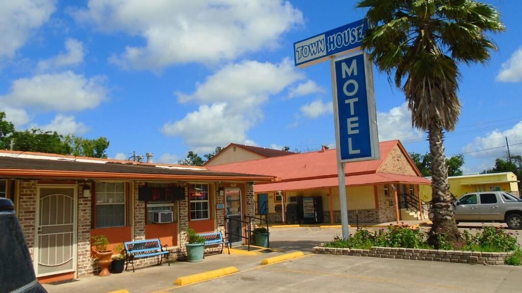 Ein Motel mit rotem Dach, blauem Schild und einer Palme davor.