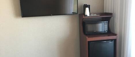 A hotel room with a flat-screen TV mounted on the wall, a microwave on a small wooden cabinet, and a patterned carpet.