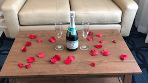 A wooden table with a bottle of champagne, two glasses, and scattered rose petals.