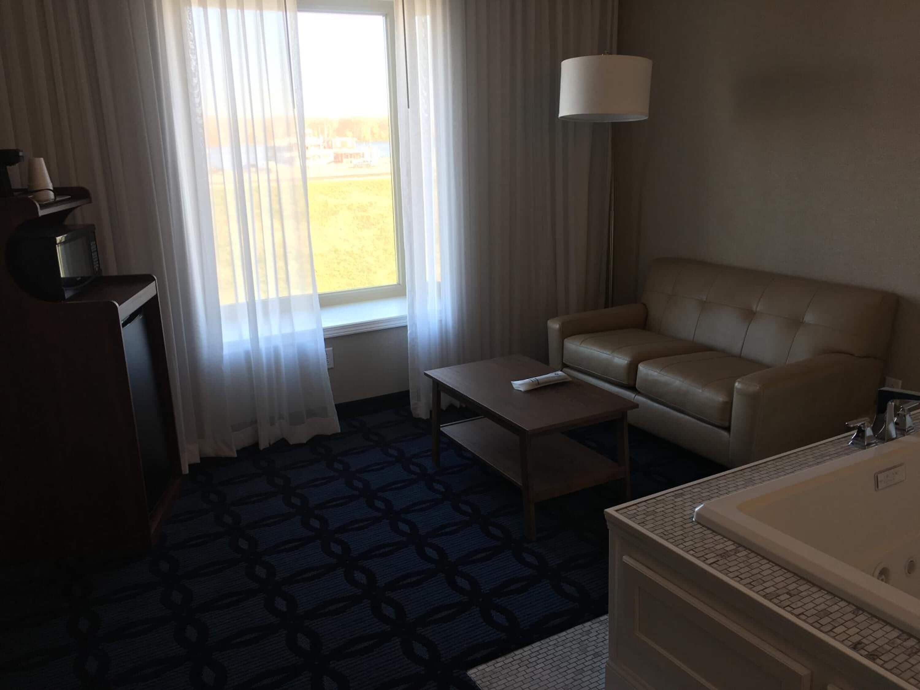 Une chambre d’hôtel équipée d’un canapé, d’une petite table, d’une lampe, d’une machine à café et d’une baignoire.