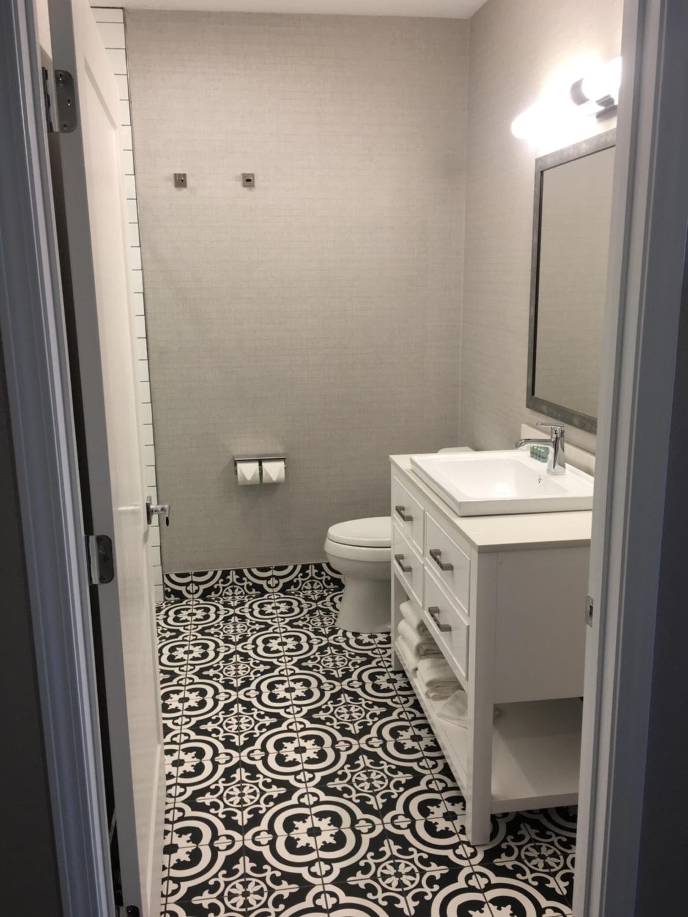 A narrow bathroom with a patterned floor, a toilet, a sink with a mirror, and a towel rack.