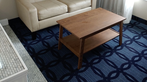 A room with a beige leather sofa, a wooden coffee table, a floor lamp, and a patterned carpet.