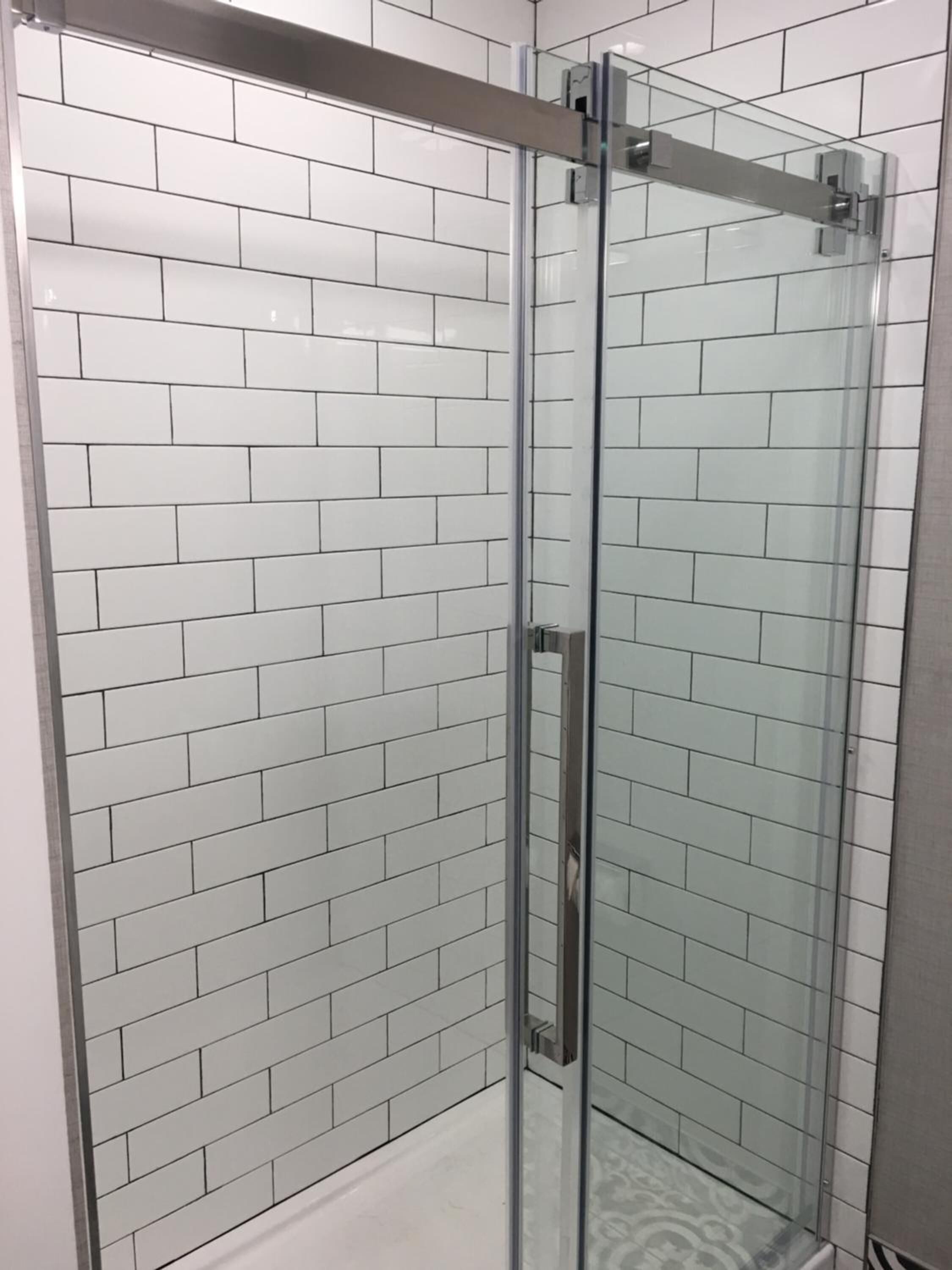 Ducha con cerramiento de vidrio y azulejos tipo metro blancos en las paredes.