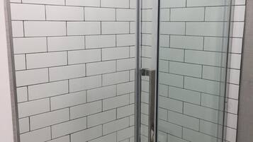 Ducha con cerramiento de vidrio y azulejos tipo metro blancos en las paredes.