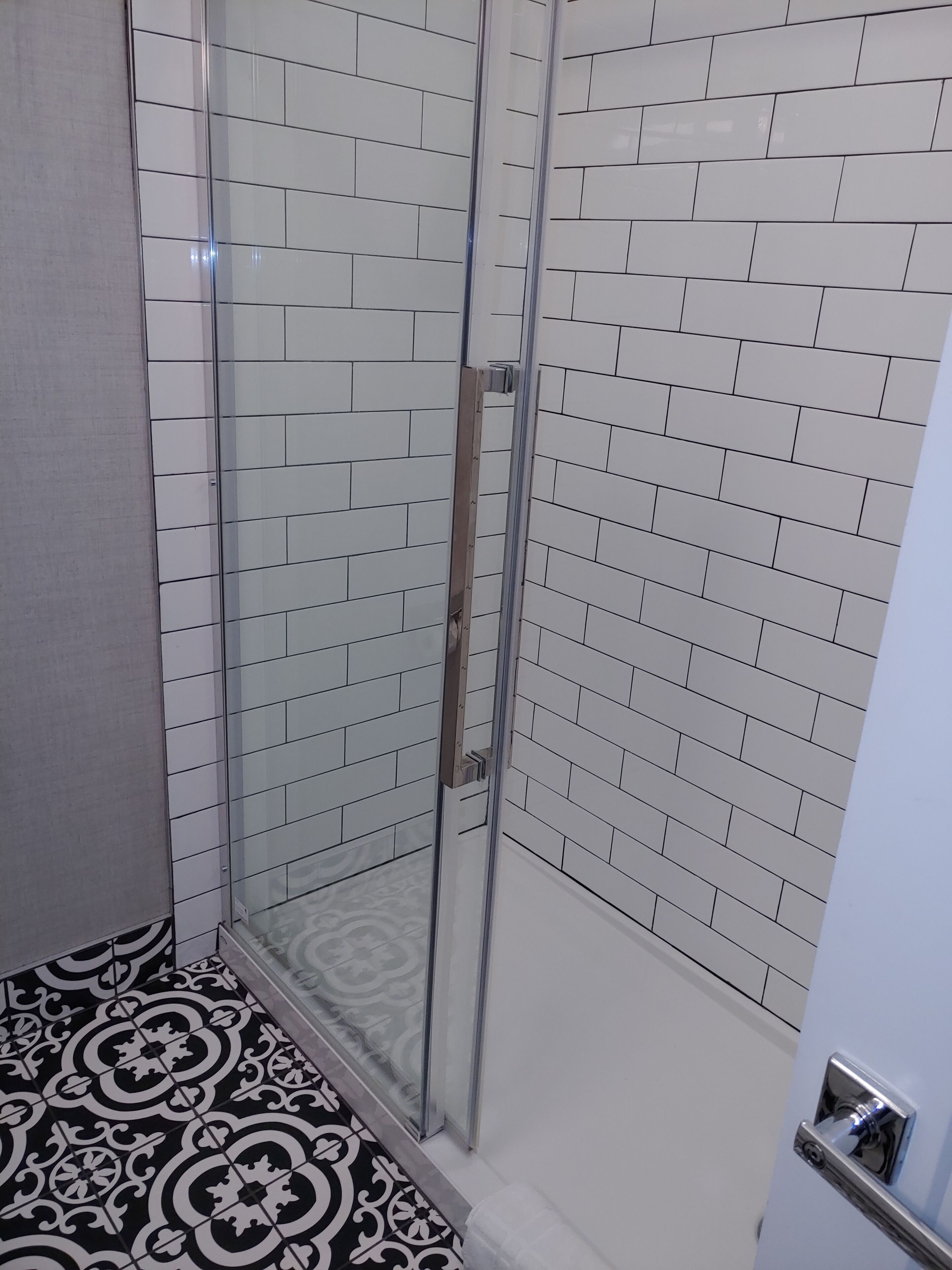 A bathroom with white subway tiles, a glass shower enclosure, and a patterned floor.