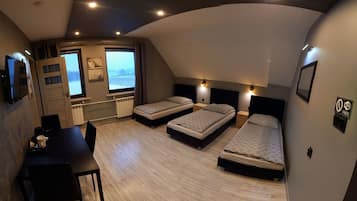 Habitación de hotel compacta con tres camas individuales, una mesa de comedor y vista al mar a través de un ventanal grande.