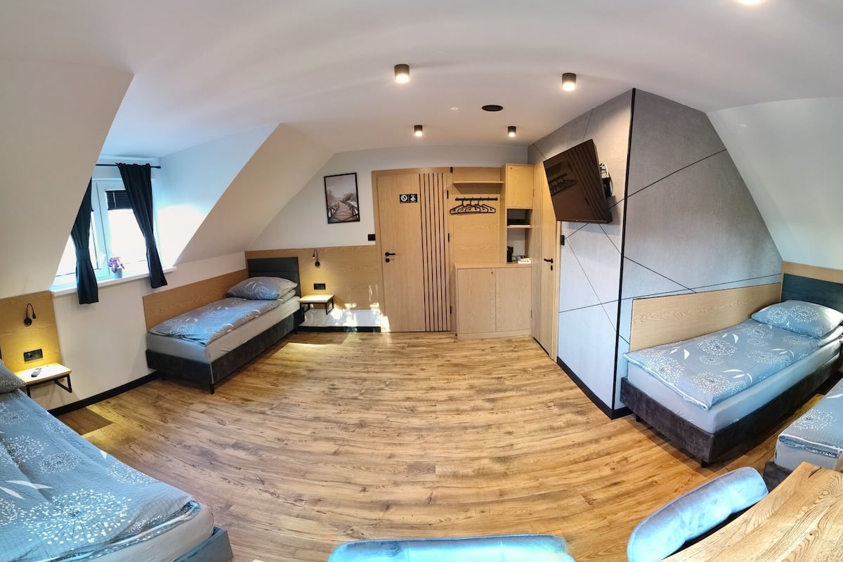 A compact, modern room with a sloped ceiling, wooden flooring, and a bed with a headboard. There is a small table and a bench.