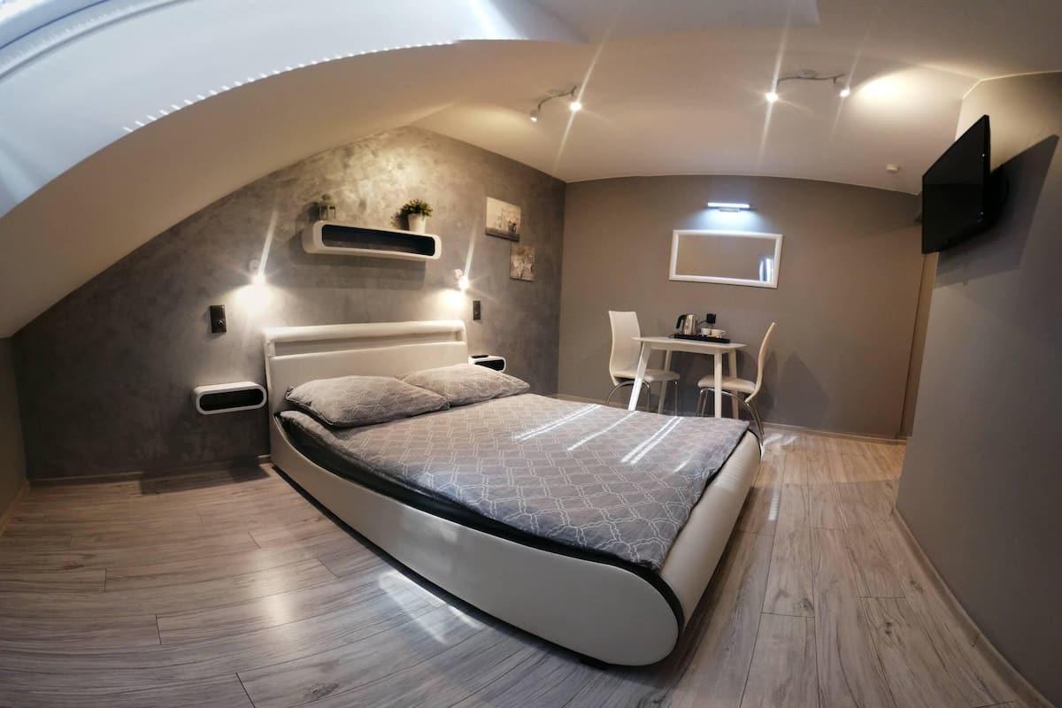 A modern bedroom with a curved ceiling, a bed, a desk, and a TV mounted on the wall.