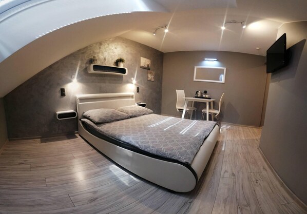 A modern bedroom with a curved ceiling, a bed, a desk, and a TV mounted on the wall.